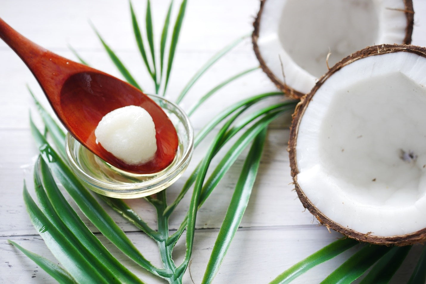 Coconut and spoon with oil setting on a palm leaf.