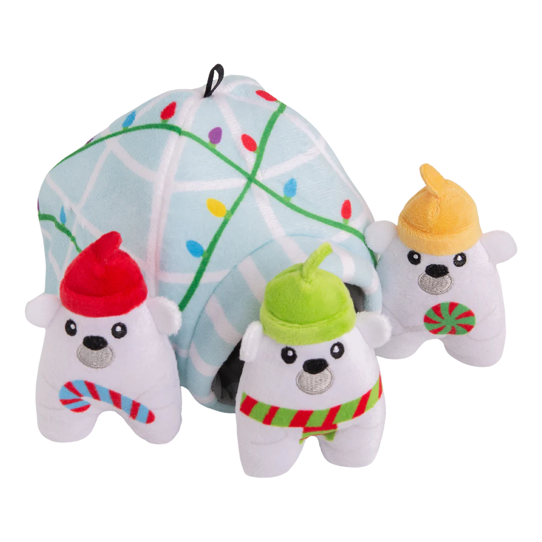 The Snugarooz Hide & Seek Igloo features three plush polar bears in festive hats and scarves, standing before a pastel blue igloo with Christmas lights. Hide treats inside for interactive, holiday fun with your pup!.