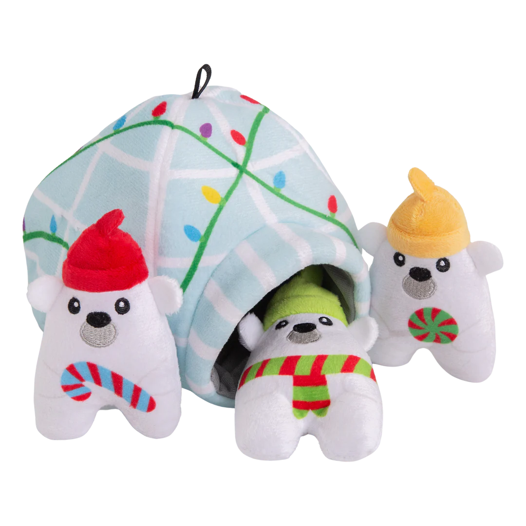 The Snugarooz Hide & Seek Igloo features three plush polar bears in festive hats and scarves, standing before a pastel blue igloo with Christmas lights. Hide treats inside for interactive, holiday fun with your pup!.