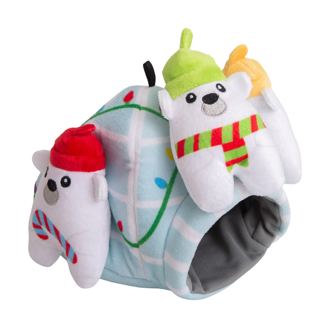 The Snugarooz Hide & Seek Igloo features three plush polar bears in festive hats and scarves, standing before a pastel blue igloo with Christmas lights. Hide treats inside for interactive, holiday fun with your pup!.