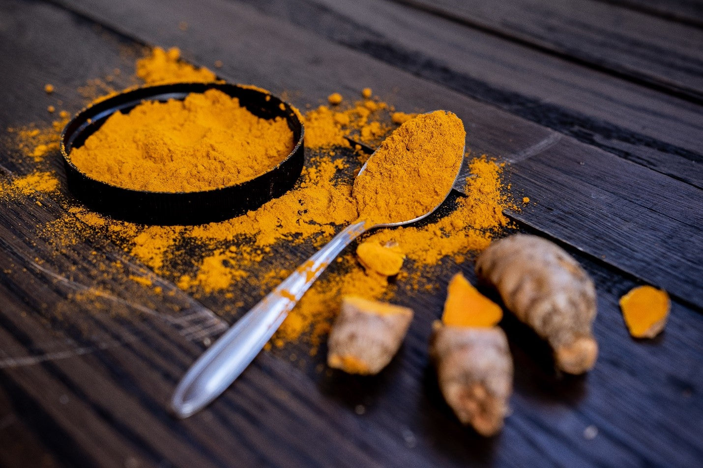 turmeric powder on a spoon and in a lid and turmeric roots
